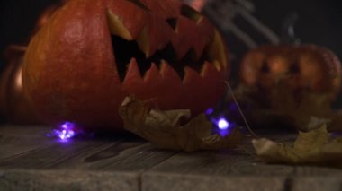 Balkabakları, kafatası, ışıklar ve kuru yapraklar ahşap masada duruyor.