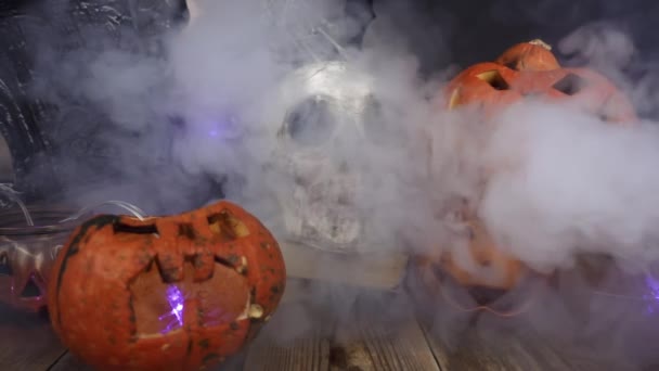 La fumée souffle lentement sur les citrouilles et le crâne debout à la table en bois — Video