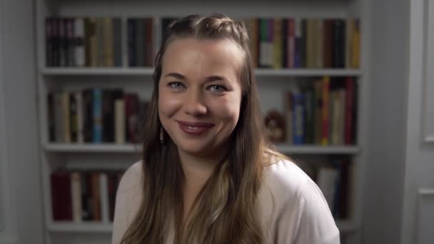 Mujer psicóloga sonrisa asiente y coquetea de acuerdo retrato contra fondo de libros — Vídeo de stock