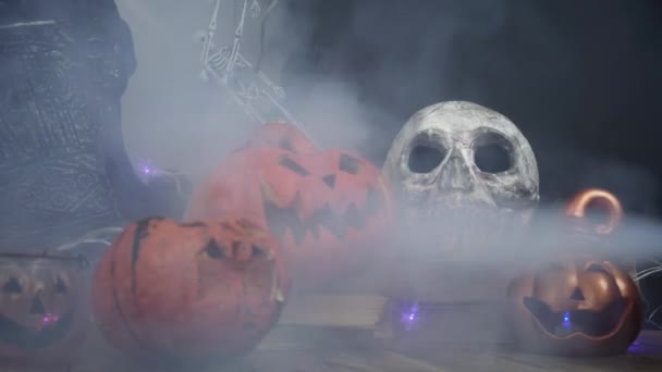 Smoke is blowing over skull and halloween pumpkins standing at the table — Stock Video