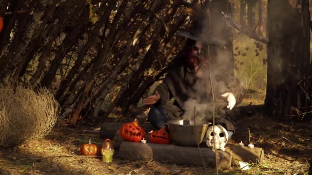 Young witch with sugar skull makeup waves hands over kettle with smoke — Stock Video