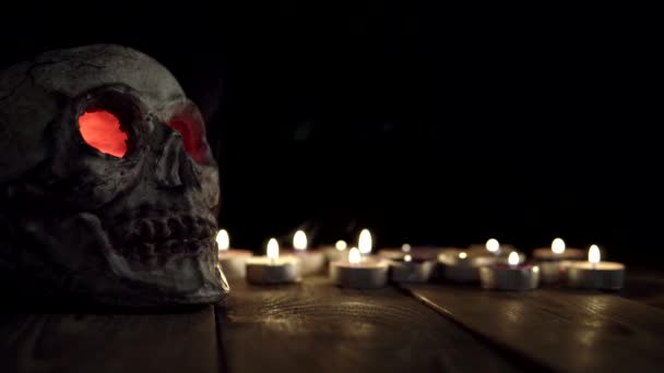 Cráneo con brillantes ojos rojos que emiten humo sobre el fondo de las velas. — Vídeos de Stock