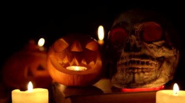 Masada elinde mumlarla duran iki balkabağı ve bir kafatası.