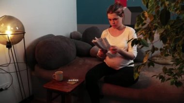 Hamile kadın oturma odasındaki kanepede oturmuş reçeteli ilaç okuyor.