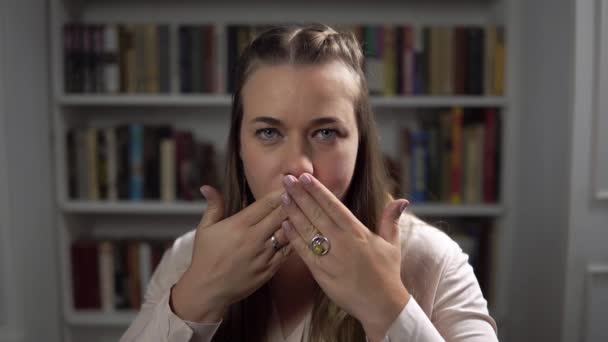 Mulher sentada na frente da estante e fecha a boca com as mãos — Vídeo de Stock