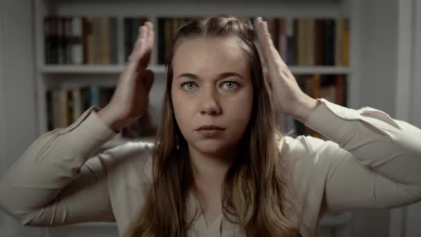 La dame est assise devant la bibliothèque et ferme ses oreilles avec les deux mains — Video