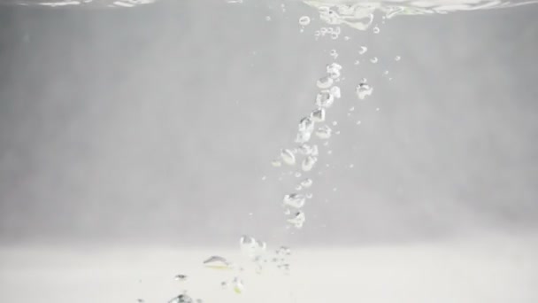 Limón amarillo cayendo en el agua con burbujas en cámara lenta. Fruta sobre fondo blanco aislado. — Vídeo de stock
