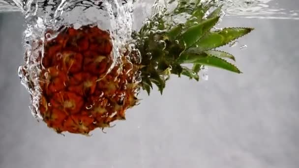 Pineapple falls into the water with splashes and bubbles in slow motion. — Stock Video