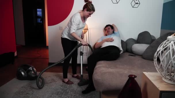 Femme enceinte nettoie son homme posé sur le canapé avec aspirateur — Video