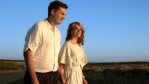 Joven pareja caucásica está caminando en un campo en un día de verano — Vídeos de Stock