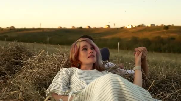 Jovem casal caucasiano está deitado no palheiro de mãos dadas e falando em campo no dia de verão — Vídeo de Stock