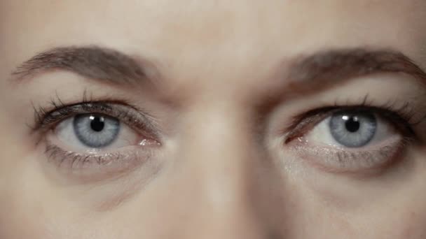 Close-up eye-portrait of a young caucasian woman who is watching seriously and directly into camera — Stock Video