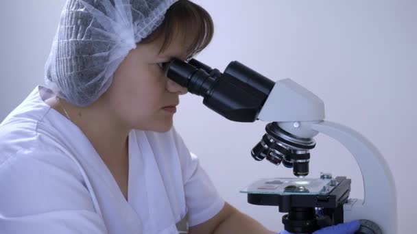 Mulher técnica de laboratório olha nos oculares de um microscópio — Vídeo de Stock