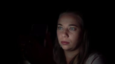 Kadın siyah arka planda duruyor ve telefona bakıyor.