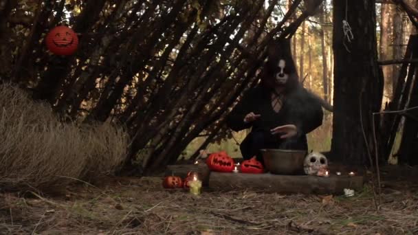 Bruxa sentada na cabana com maquiagem de crânio de açúcar move as mãos no vapor — Vídeo de Stock