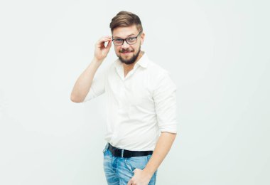 Beyaz gömlek ve gri arka plan üzerinde rahat kıyafetler giymiş gözlüklü genç bir adam portresi