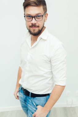 Beyaz gömlek ve gri arka plan üzerinde rahat kıyafetler giymiş gözlüklü genç bir adam portresi