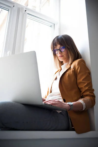 Beautiful woman designer freelancer in eyeglasses wearing casual using laptop in white office