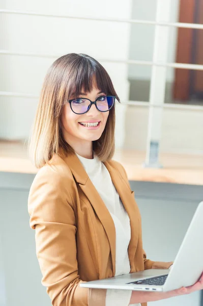 Beautiful woman designer freelancer in eyeglasses wearing casual using laptop in white office