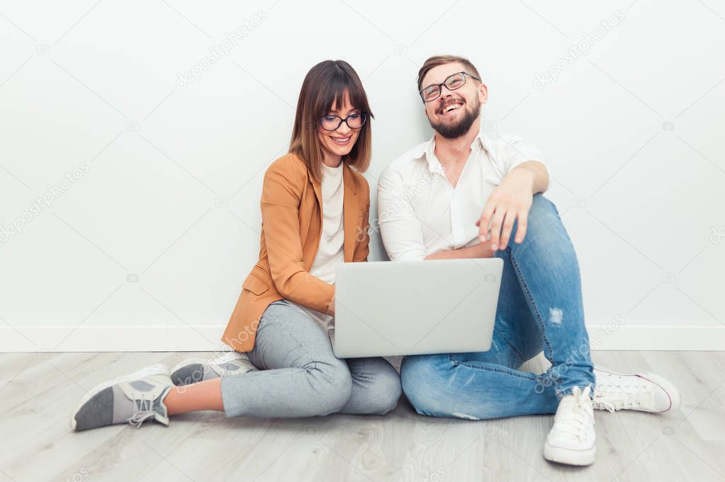 Two young coworkers dressed casual using laptop in white interior