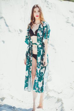 Kumsalda yürüyen güzel genç bir kadın, yeşil çöl kıyafetleri.