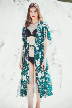 Kumsalda yürüyen güzel genç bir kadın, yeşil çöl kıyafetleri.