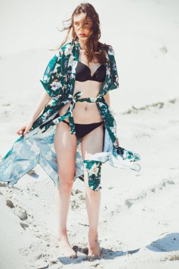 Yeşil mayo beyaz kum plaj üzerinde poz çekici ince kız. Genç kadın tatil kumlu okyanus sahilinde bikin dayanmaktadır. Kavram seyahat, mayo