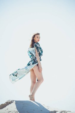 Yeşil mayo beyaz kum plaj üzerinde poz çekici ince kız. Genç kadın tatil kumlu okyanus sahilinde bikin dayanmaktadır. Kavram seyahat, mayo