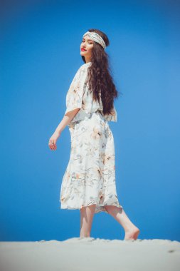 Plaj elbisesi ve kafasında kurdele olan güzel bir kadın. Çölde yürürken.