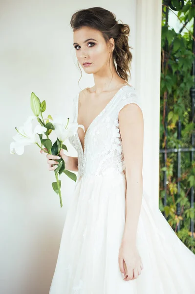 結婚式の前に白い家の近くを歩く光の長い白いドレスで結婚式の花束を持つ若いエレガントな女性 — ストック写真