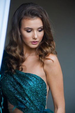 Güzel saçlı ve makyajlı genç bir kadının üzerinde şık bir zümrüt gece elbisesi.