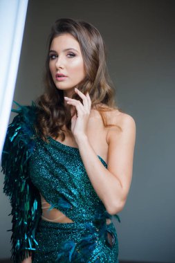 Güzel saçlı ve makyajlı genç bir kadının üzerinde şık bir zümrüt gece elbisesi.