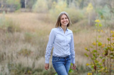 Sıradan giyinmiş, kuru bir alanda gülümseyen bir iş kadını.