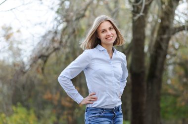 Sıradan giyinmiş, kuru bir alanda gülümseyen bir iş kadını.