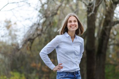 Sıradan giyinmiş, kuru bir alanda gülümseyen bir iş kadını.