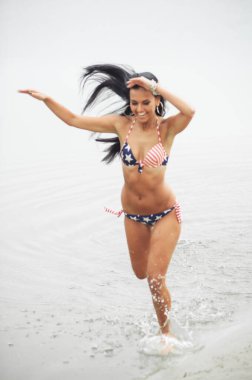 Bağımsızlık gününde kumsalda Amerikan bayrağıyla gülümseyen güzel bir genç kadın.