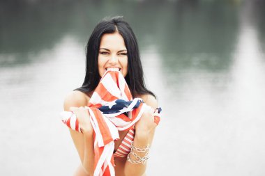 Bağımsızlık gününde kumsalda Amerikan bayrağıyla gülümseyen güzel bir genç kadın.
