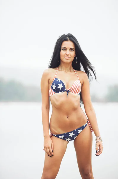 独立記念日にビーチでアメリカ国旗を持つ美しい笑顔の若い女性 — ストック写真