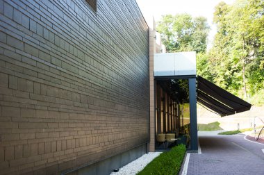 Geniş panoramik pencereleri ve peyzajı olan modern bir binanın ön cephesi.