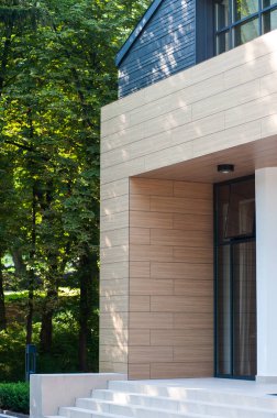 Geniş panoramik pencereleri ve peyzajı olan modern bir binanın ön cephesi.