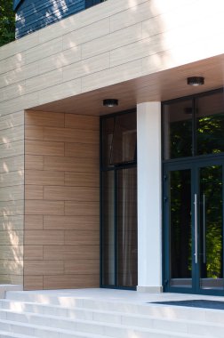 Geniş panoramik pencereleri ve peyzajı olan modern bir binanın ön cephesi.