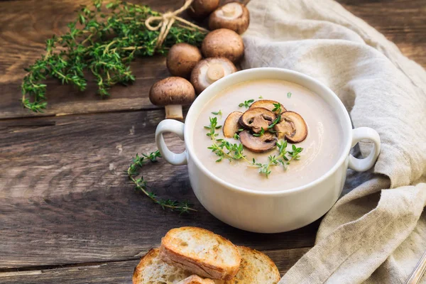 Creamy mushroom soup with champignons on rustic wooden background.