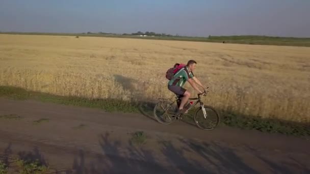 Un ciclista pedala lungo la strada tra campi agricoli — Video Stock