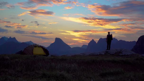 Um homem perto da tenda olha para o amanhecer — Vídeo de Stock