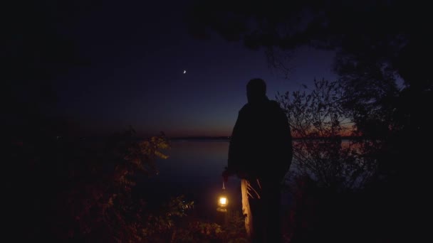 Uomo con una lampada sulla riva del fiume — Video Stock