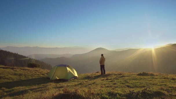 Um homem está perto de uma tenda nas montanhas — Vídeo de Stock