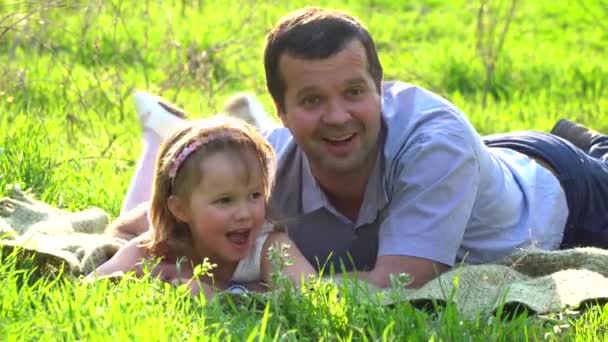 Счастливые отец и дочь отдыхают на траве — стоковое видео