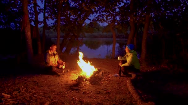 Un hombre y una mujer cerca de un incendio en el bosque nocturno — Vídeo de stock