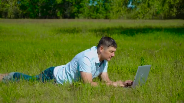 Uomo d'affari lavora dietro un computer portatile sdraiato sull'erba — Video Stock