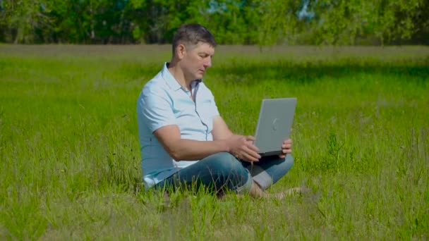 Uomo d'affari lavora dietro un computer portatile seduto sull'erba — Video Stock